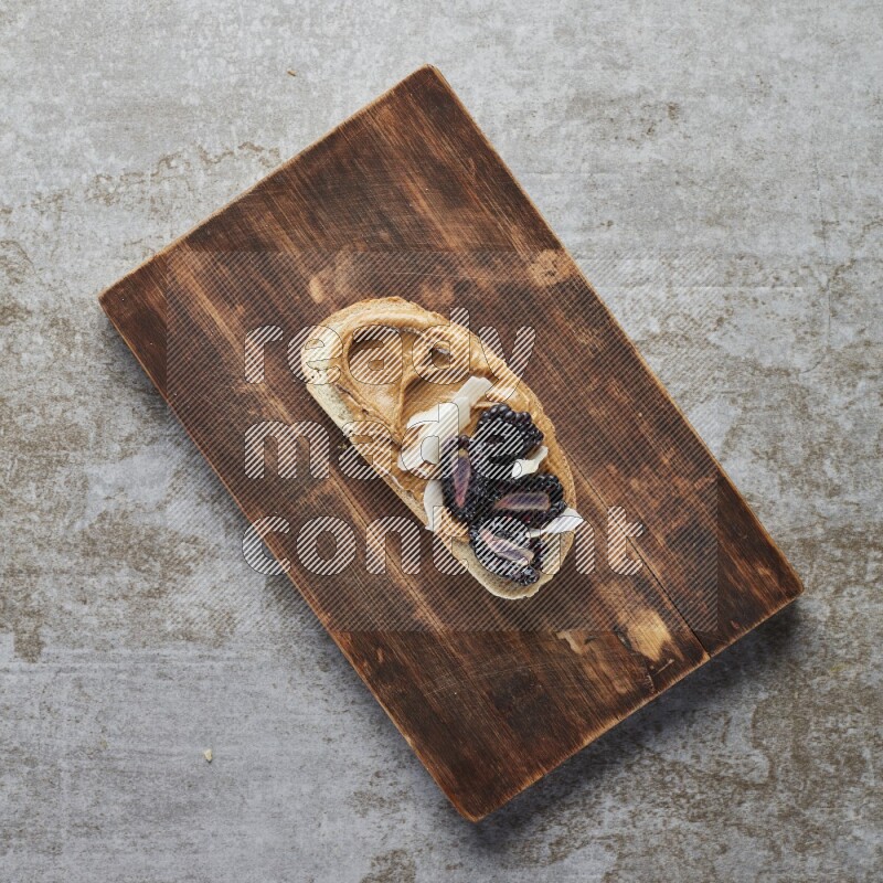 open faced peanut butter sandwich with blackberries  and coconut flakes on a  grey textured background