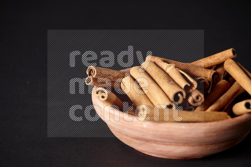 Cinnamon Sticks in a wooden bowl on black background