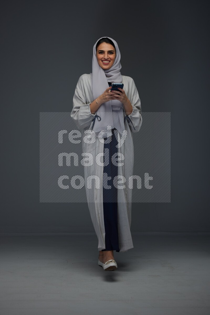 A Saudi woman Texting wearing Grey Abaya on a grey background