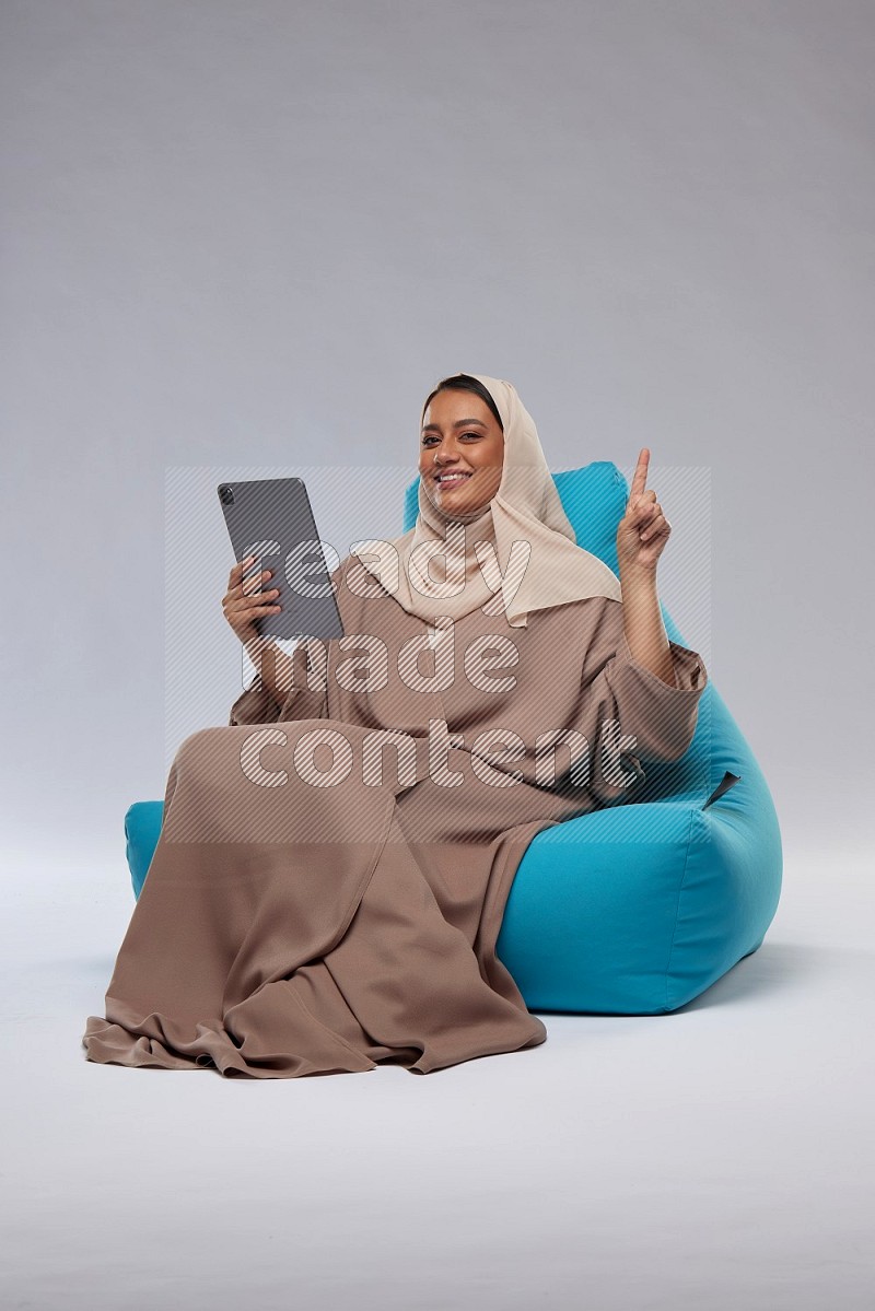 A Saudi woman sitting on a blue beanbag and working on tablet