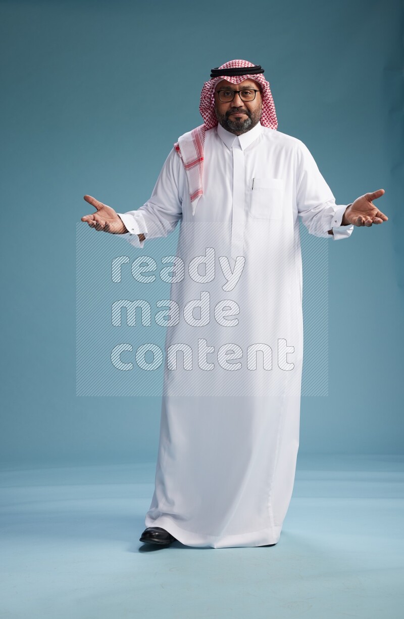 Saudi Man with shimag Standing Interacting with the camera on blue background