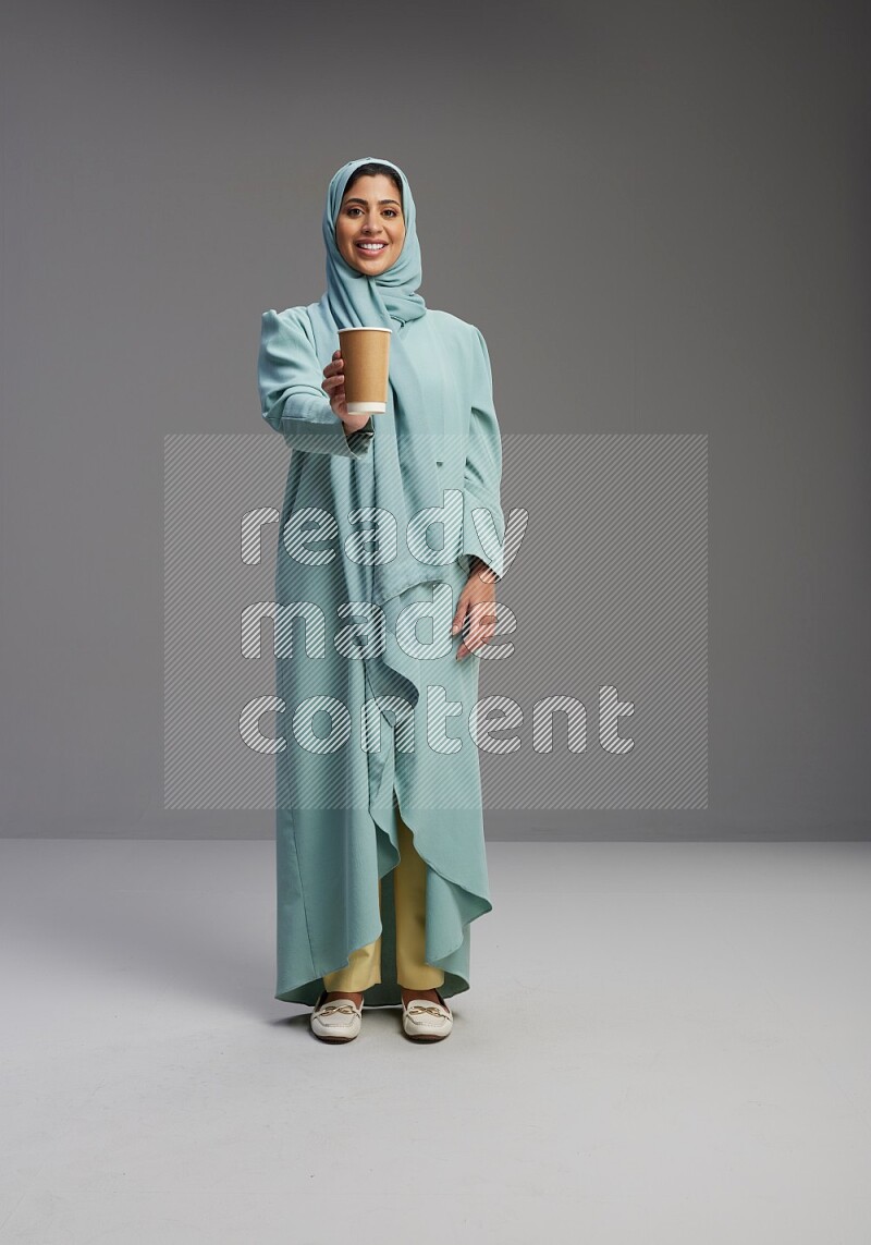 Saudi Woman wearing Abaya standing  holding paper cup on Gray background