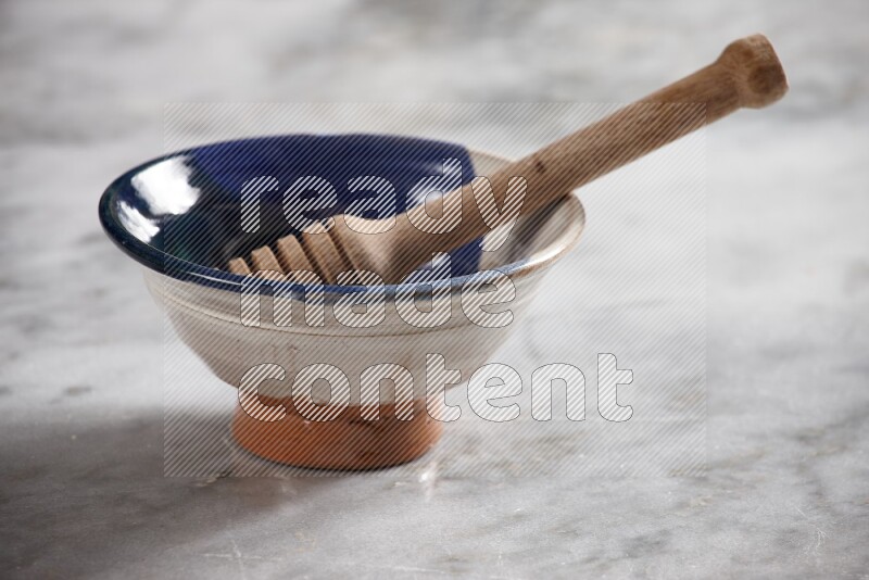Multicolored pottery bowl with wooden honey dipper in it on grey marble background