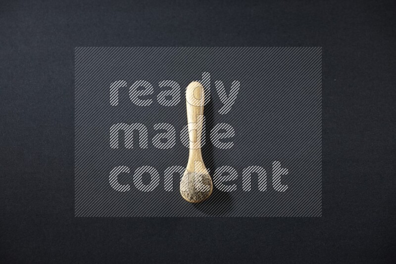 ملعقة خشبية ممتلئة ببودرة الهيل على خلفية سوداء