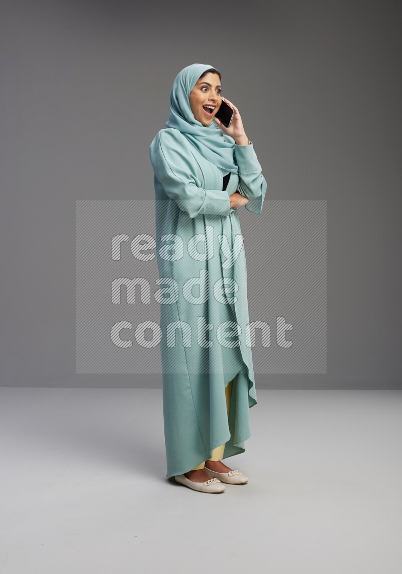 Saudi Woman wearing Abaya standing talking on phone on Gray background