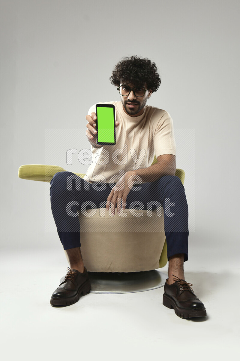 A man wearing casual sitting on a chair showing a phone screen on white background