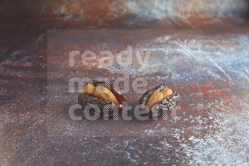 two almond stuffed madjoul dates on a rustic reddish background