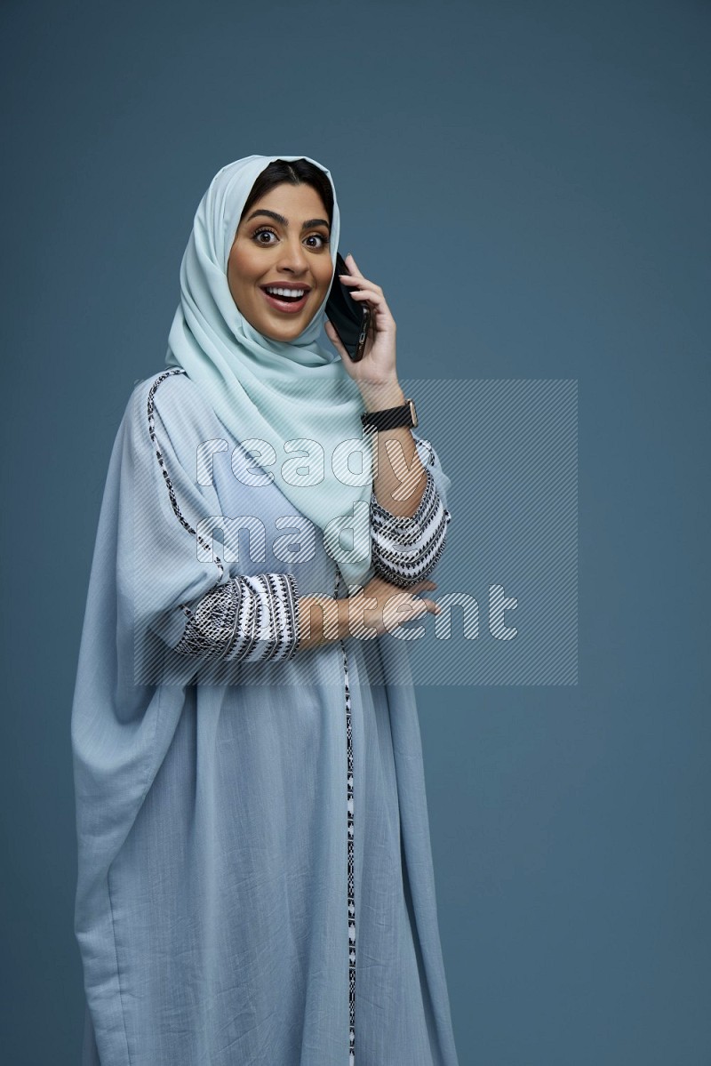 A Saudi woman having a Call in a blue background wearing blue Abaya with hijab