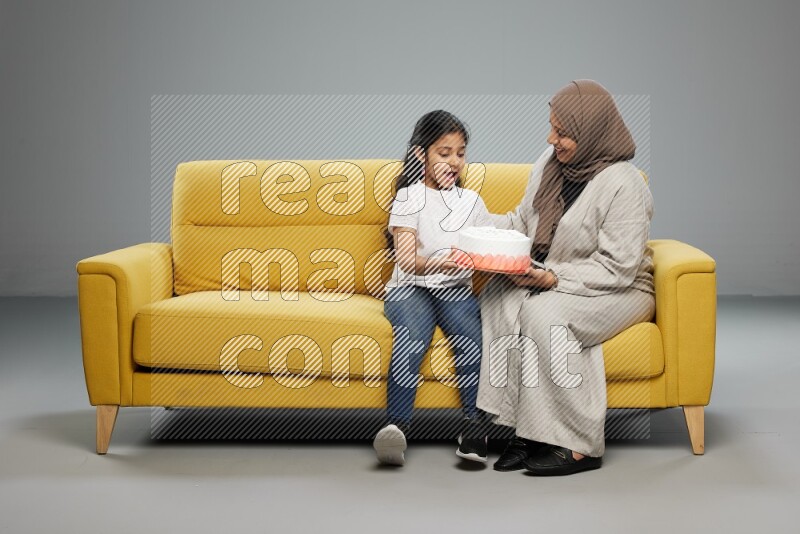 A girl sitting giving a cake to her mother on gray background