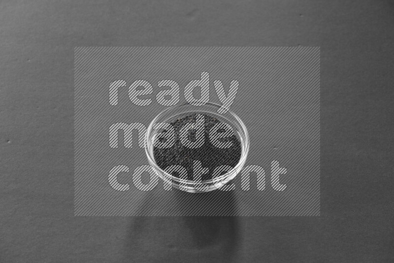 A glass bowl full of black seeds on black flooring