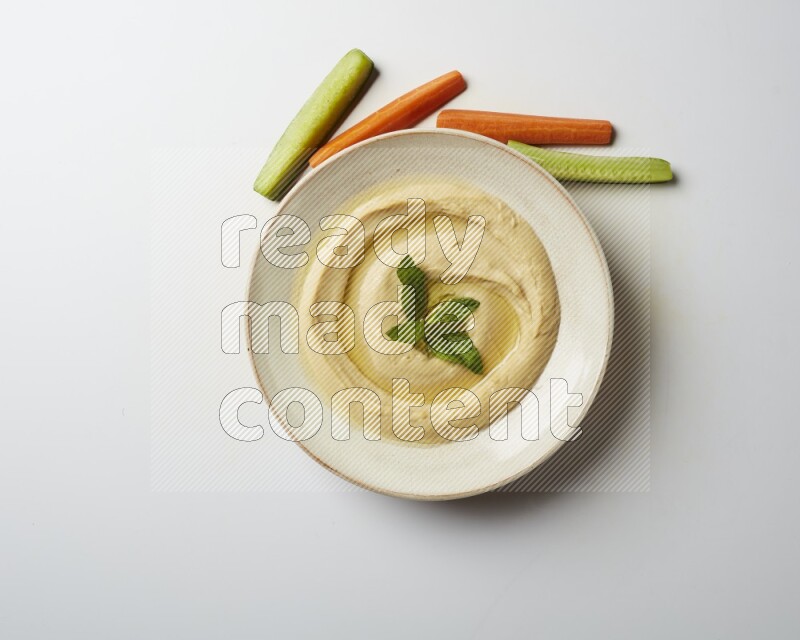 Hummus in a pottry plate garnished with mint  on a white background