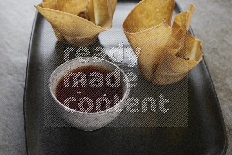 wonton cups with soy sauce ramkin on rectangle dark grey ceramic plate on grey textured counter top