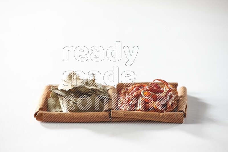 مربعان من أعواد القرفة ممتلئان بالفلفل الحار المجفف وأوراق الغار علي خلفية بيضاء