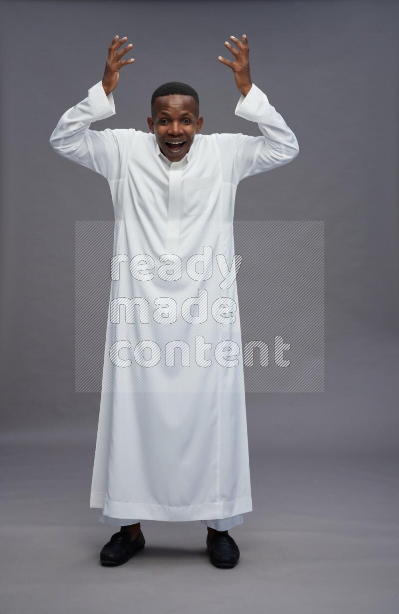 Saudi man wearing thob standing hands behind head on gray background
