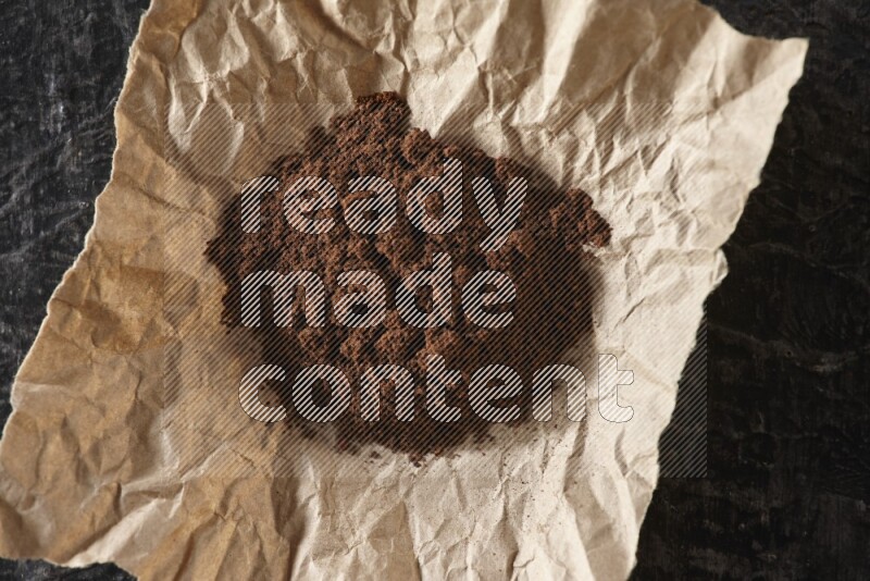 Cloves powder in crumpled piece of paper on a textured black flooring