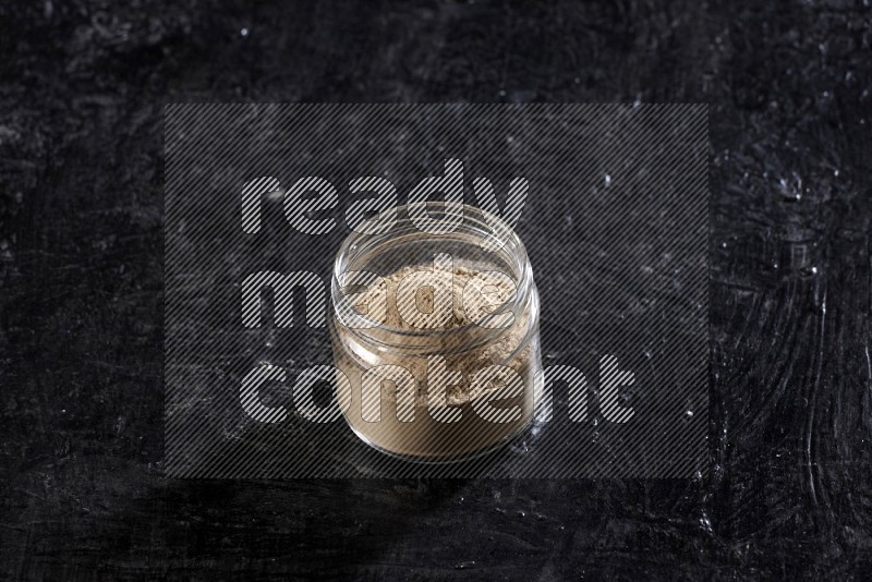 A glass jar full of garlic powder on a textured black flooring