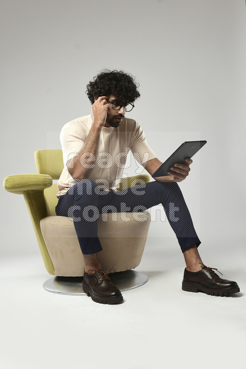 رجل يرتدي ملابس كاجوال يجلس علي كرسي و يتصفح تابلت علي خلفية بيضاء