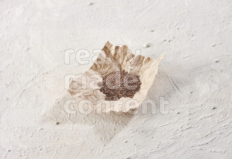A crumpled piece of paper full of flax seeds on a textured white flooring