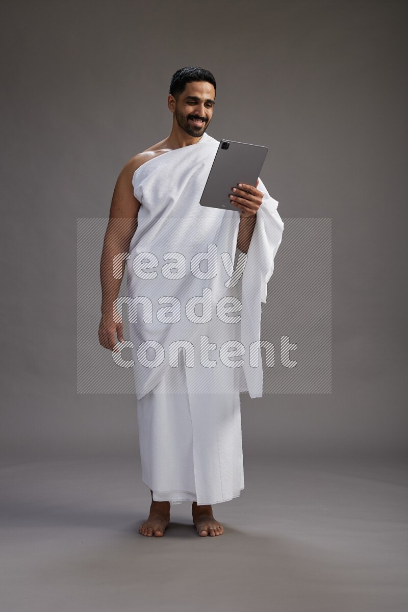 A man wearing Ehram and holding a tablet on gray background