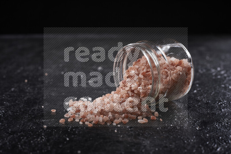 A glass jar full of coarse himalayan salt crystals on black background