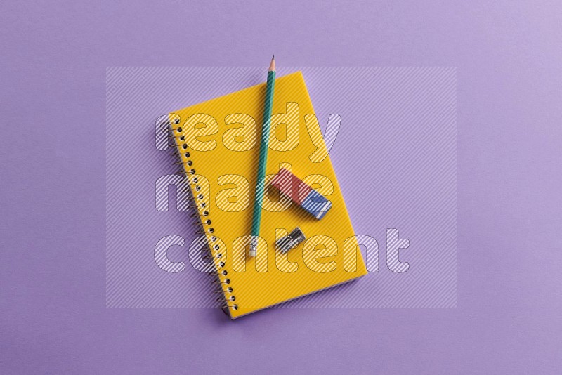 A yellow notebook with school supplies on purple background (Back to school)