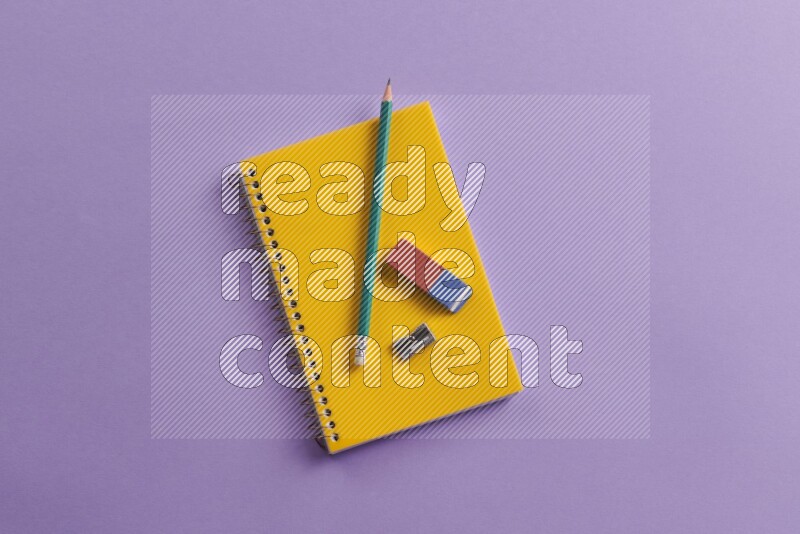 A yellow notebook with school supplies on purple background