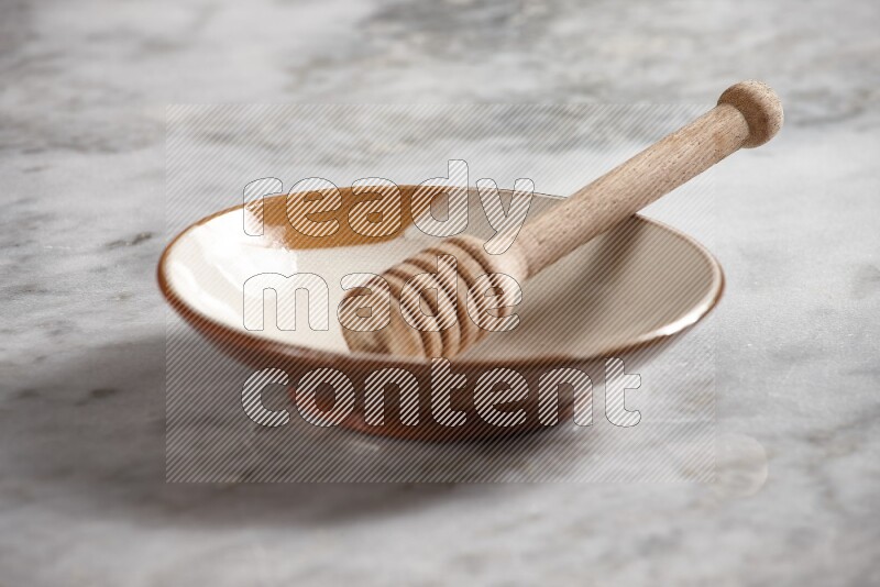 Multicolored pottery plate with wooden honey dipper in it on grey marble background
