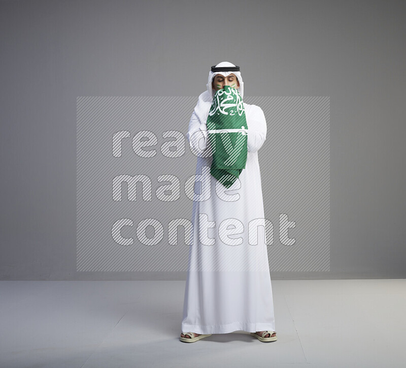 رجل سعودي يرتدي ثوب وشماغ ويحمل العلم السعودي