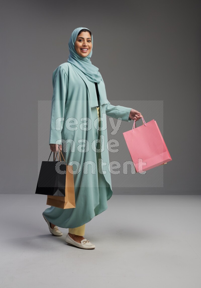 Saudi Woman wearing Abaya standing holding shopping bag on Gray background