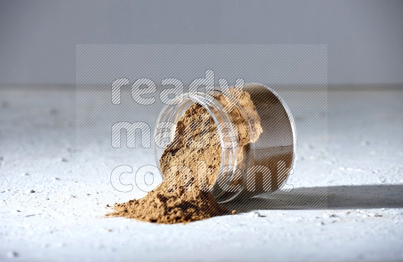 A flipped glass jar full of allspice powder and powder spilled out of it on a textured white flooring