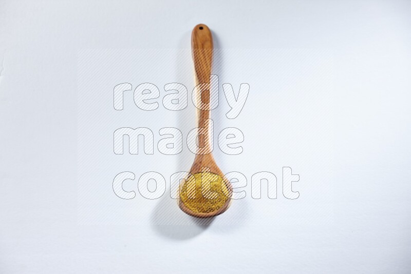 A wooden ladle full of turmeric powder on white flooring