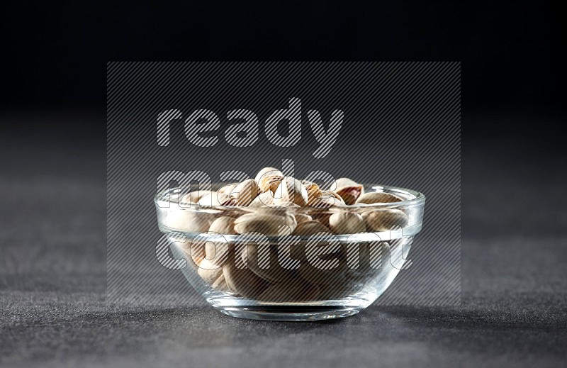 A glass bowl full of pistachios on a black background in different angles