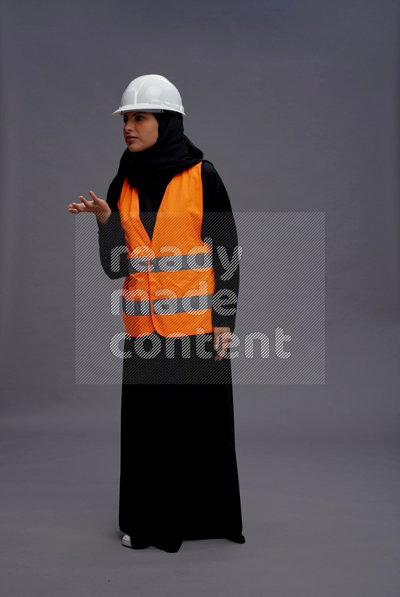 Saudi woman wearing Abaya with engineer vest standing interacting with the camera on gray background