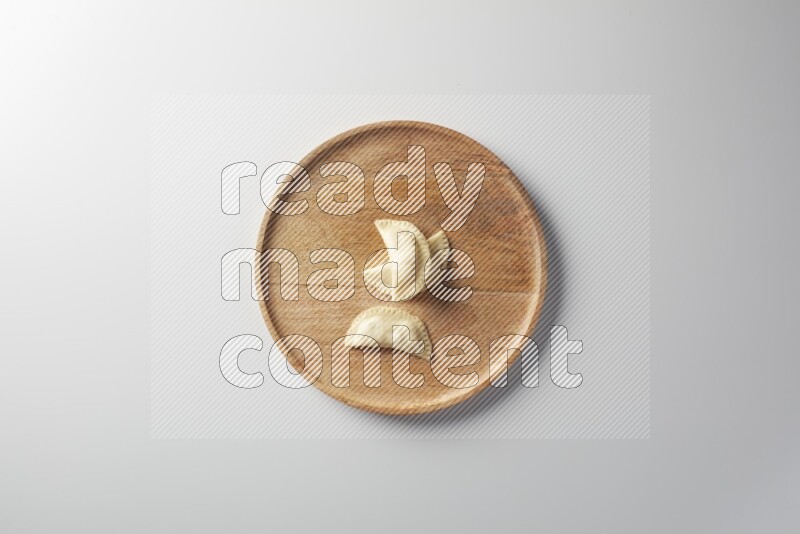 Three Sambosas on a wooden round plate on a white background