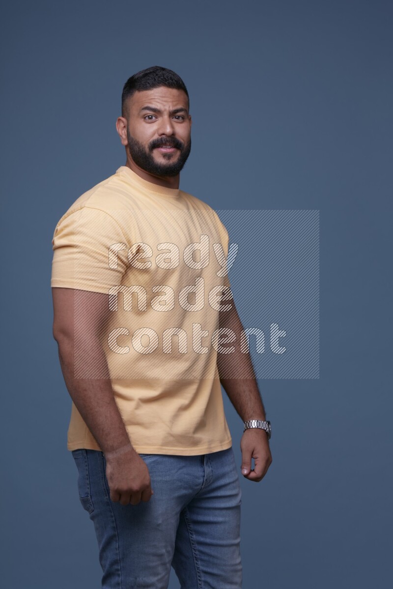 A man posing in a blue background wearing a yellow shirt