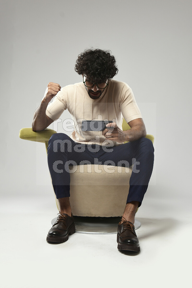 A man wearing casual sitting on a chair gaming on the phone on white background