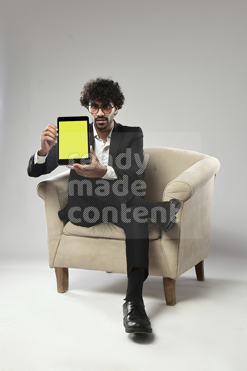A man wearing formal sitting on a chair showing a tablet screen on white background