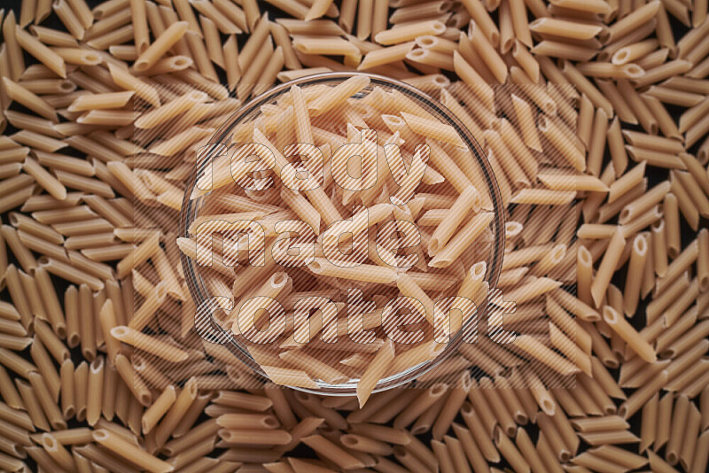 Mini penne pasta in a glass bowl on black background
