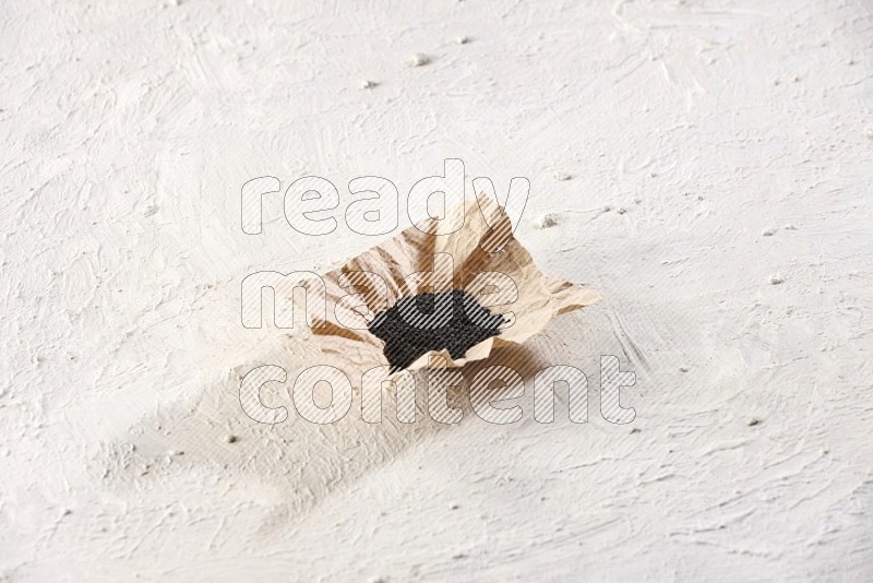 A crumpled piece of paper full of black seeds on a textured white flooring in different angles