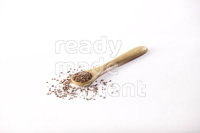 A wooden spoon full of flax seeds on a white flooring