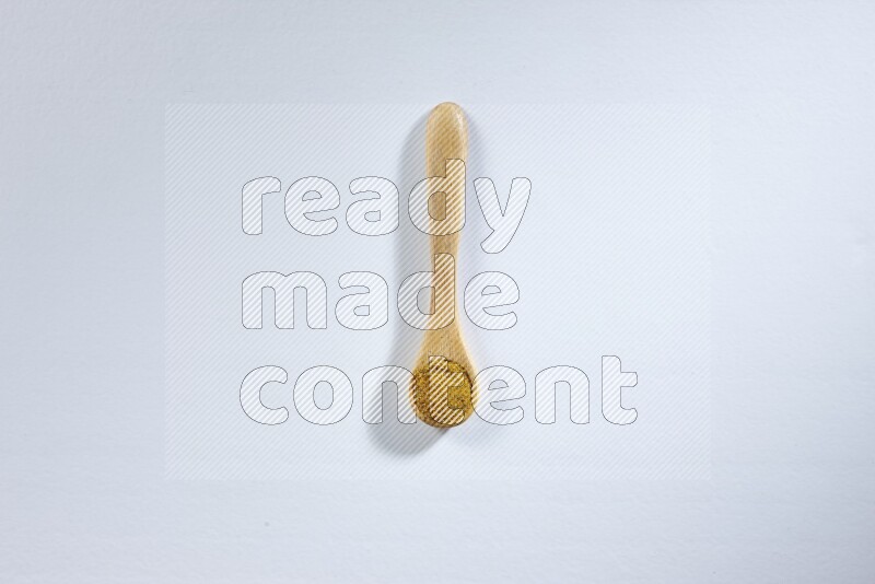 A wooden spoon full of turmeric powder on white flooring