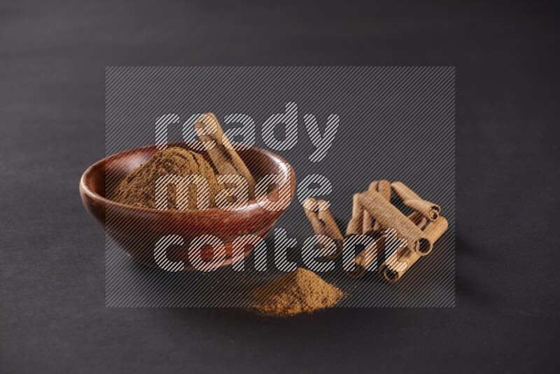 Cinnamon powder in a wooden bowl with a cinnamon sticks on black background
