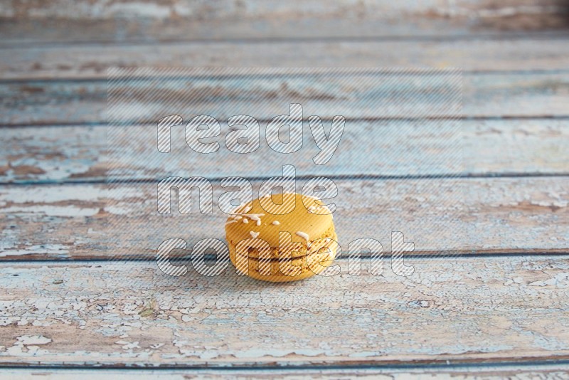 45º Shot of Yellow Piña Colada macaron on light blue wooden background