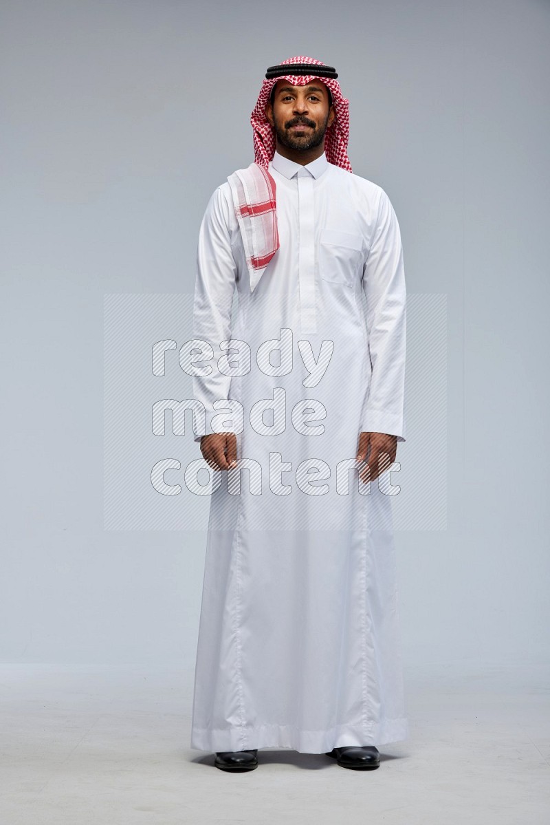 Saudi man Wearing Thob and shomag standing interacting with the camera on Gray background