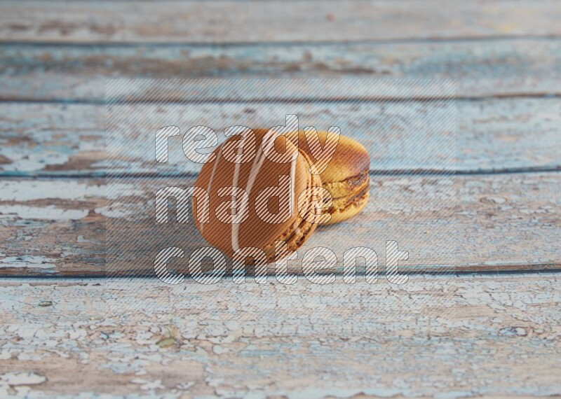 45º Shot of of two assorted Brown Irish Cream, and Yellow Crème Brulée macarons on light blue background