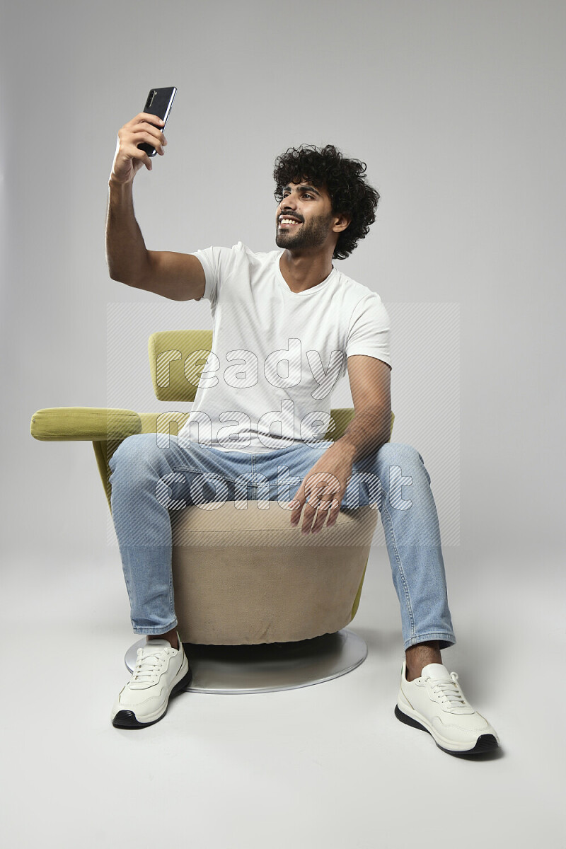 A man wearing casual sitting on a chair taking a selfie on white background