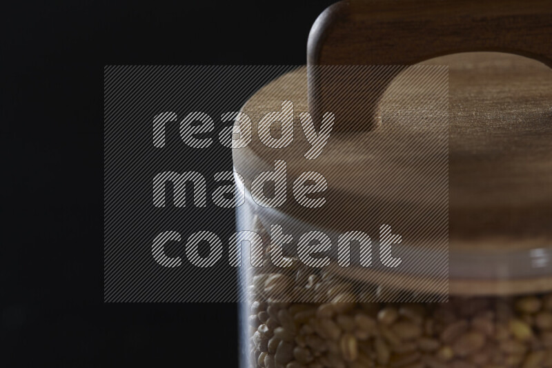 Hulled wheat in a glass jar on black background