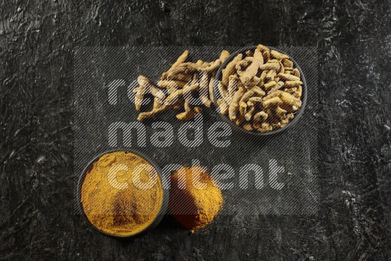 وعاءان من الفخار باللون الأسود، أحدهما ممتلئ ببودرة الكركم والآخر ممتلئ بأصابع كاملة من الكركم المجفف على خلفية سوداء