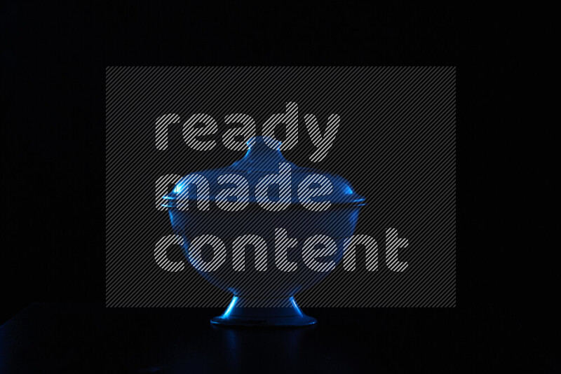 A vintage metal pot with colored rim light against black background