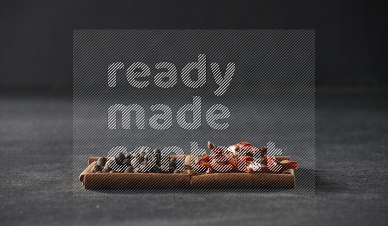 مربعان من أعواد القرفة ممتلئان بالفلفل الحار المجفف وحبوب بهار الفلفل الحلو علي خلفية سوداء